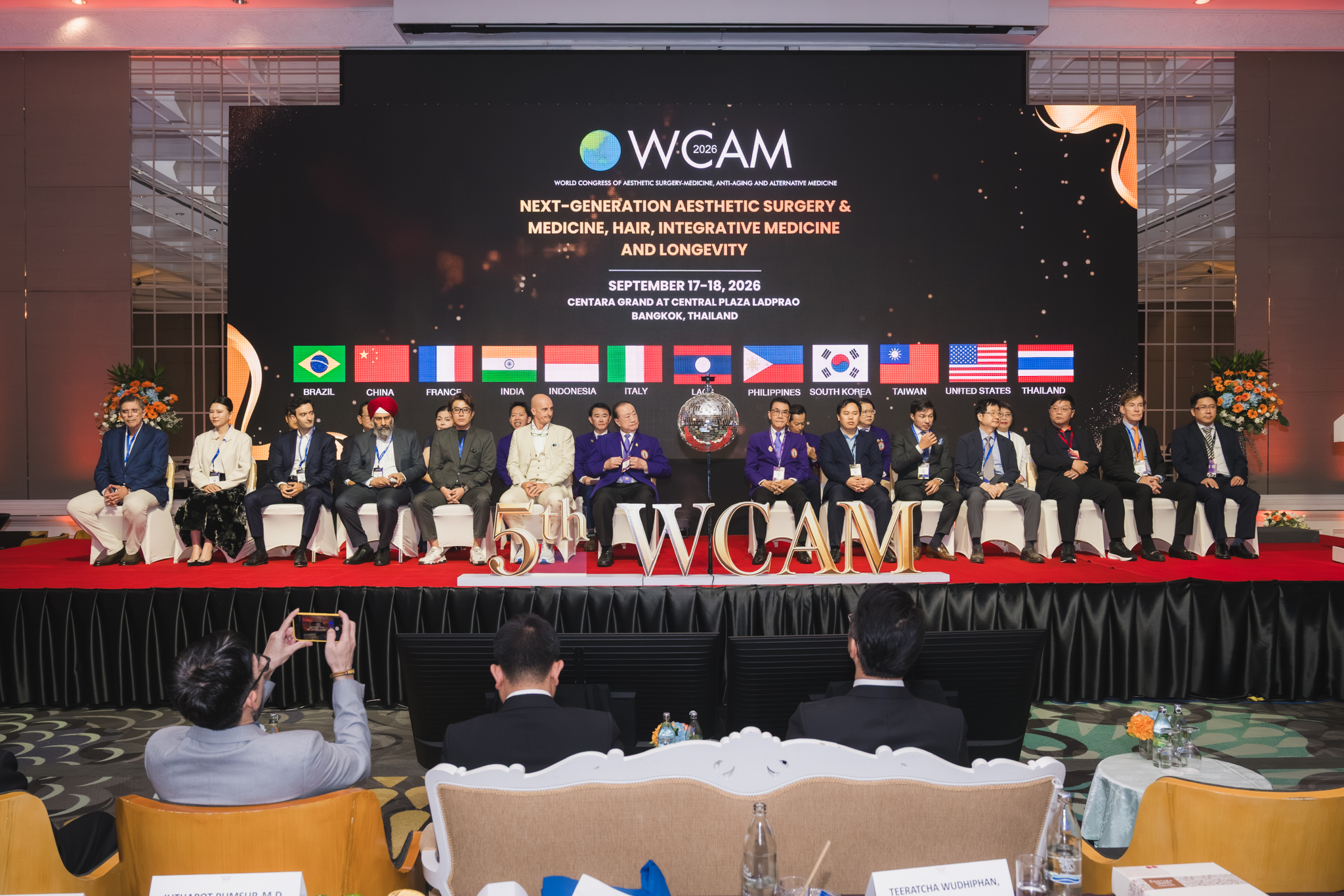 Relatori sul palco durante la cerimonia di apertura del WCAM 2026 a Bangkok, con le bandiere dei Paesi partecipanti